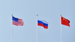 Flags of the United States, China and the Russian Federation on flagpoles against a blue background