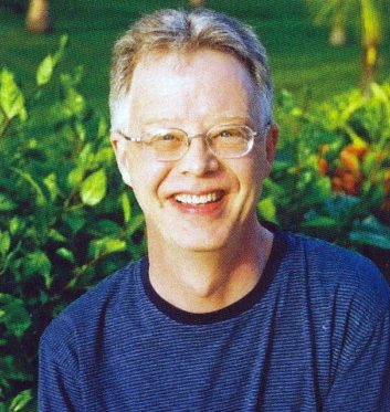 Jeff Goode stands smiling in front of shrubbery.