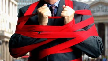 A photo of a man in a suit fighting red tape, showing only his torso and arms.