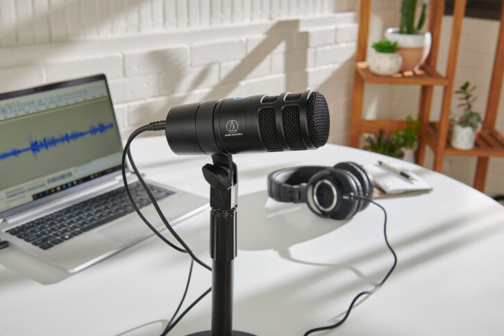 Audio-Technical AT2040USB microphone, a short black dynamic mic, shown on a tabletop stand in front of a laptop.