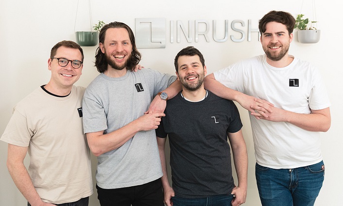 The four partners of Inrush Broadcasting stand in front of the company logo in a lobby. 