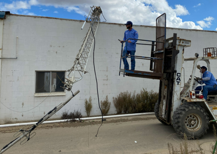 A man on a forklift inspects a small radio tower that has fallen partly off of a building roof.