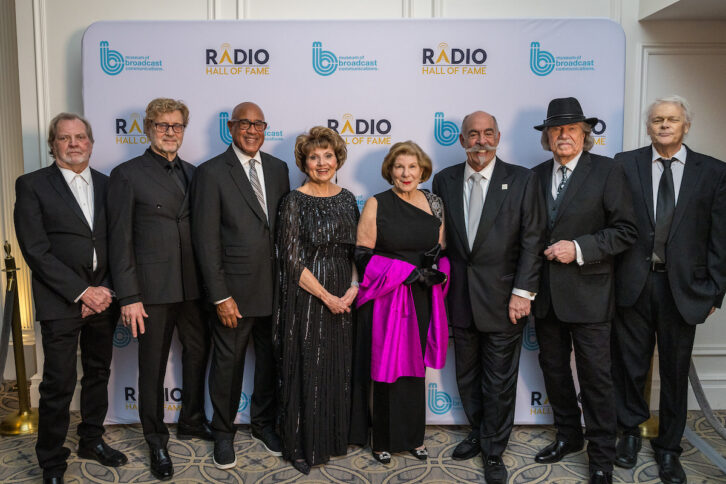 Radio Hall of Fame 2023 inductees pose as a group in front of an event banner. From left: Gerry House, Shadoe Stevens, Charles Warfield, Deborah Parenti, Nina Totenberg, John DeBella, Pat St. John, and Bob Rivers.