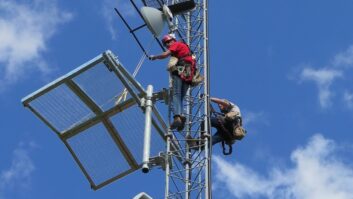 Two crewmembers climb a broadcast tower