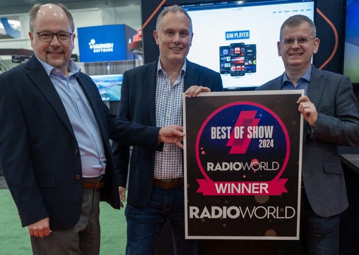 Three men stand in a booth at the NAB Show, holding a placard proclaiming a winner of the Best of Show Award