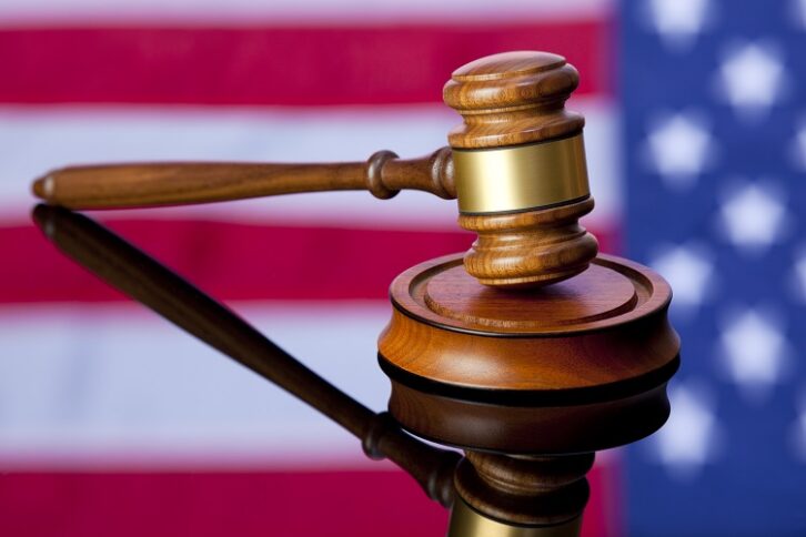 A judicial gavel sitting on a tabletop in which the colors of the US flag are reflected