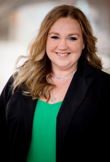 A woman wearing a dark blazer and a green top smiles at the camera.