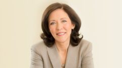 A woman wearing a business blazer smiles at the camera.