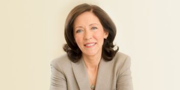 A woman wearing a business blazer smiles at the camera.