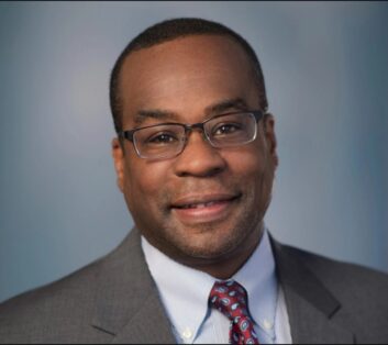headshot of a main in a grey business suit and red tie