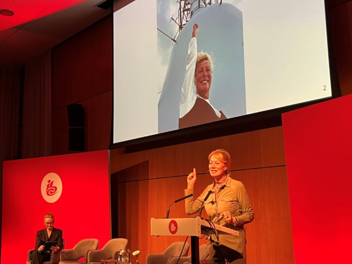 Jacqueline Bierhorst speaking at IBC2024, with a photo of her visit to the top of the broadcast tower in the south of Amsterdam.