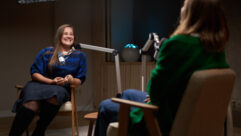 Smiling female podcast host sitting on chair and listening to funny story from guest in modern studio