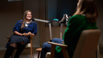 Smiling female podcast host sitting on chair and listening to funny story from guest in modern studio