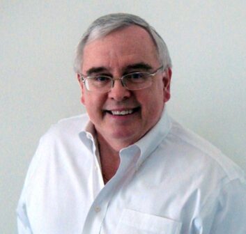 A man in an open-necked white button-down shirt smiles at the camera