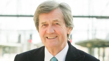 A man in a suit and tie is standing outdoors smiling at the viewer