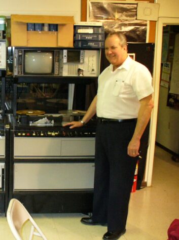 A man stands in front of several pieces of audio equipment