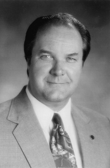 A man wearing a suit and tie smiles at the camera.
