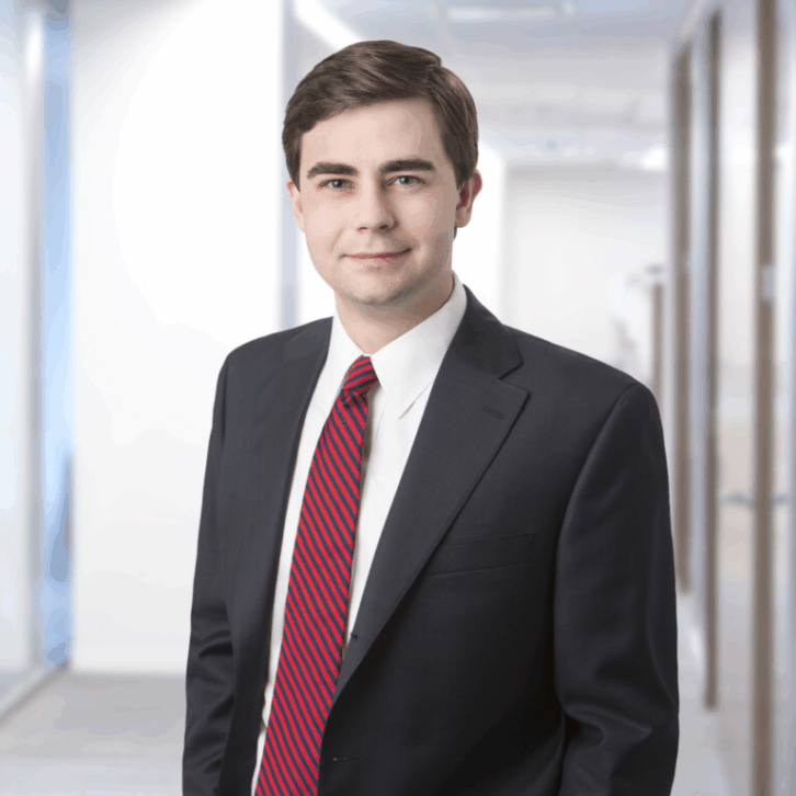 A main in a dark suit, white shirt and red tie smiles at the viewer