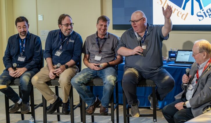 Several men sit on stools for a roundtable discussion