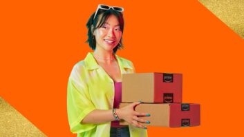 A woman in casual clothing smiles while holidng two boxes with the Amazon logo.