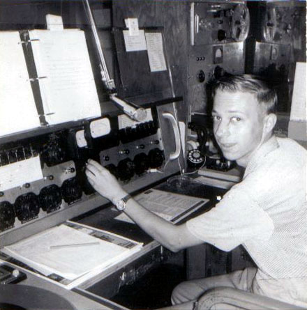 A young man is shown sitting at a broadcast console and microphone in the 1960s