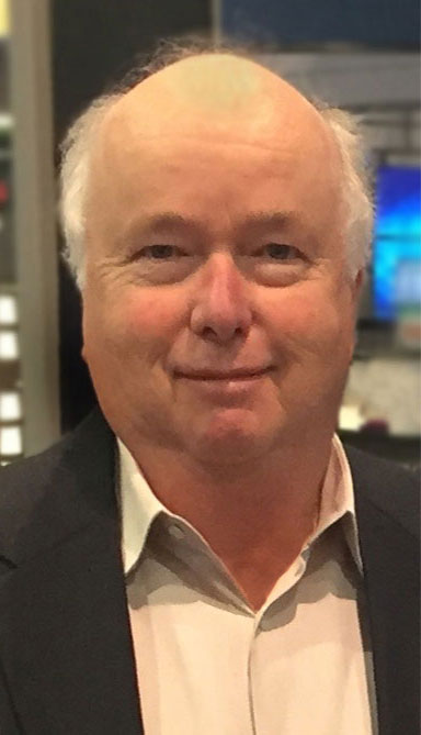A man in a business jacket and open-necked shirt smiles at the camera