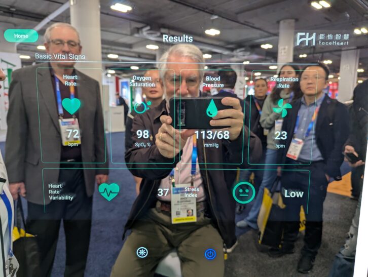 John Garziglia, with New Jersey radio broadcaster group owner Bob McAllan of Press Communications LLC to the left, reflected in the CardioMirror at CES 2025 taking a photo of his instantly rendered health measurements. 