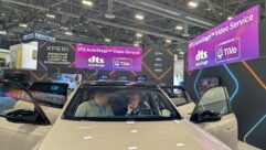 Attendees sit in a car on exhibit in the Xperi booth at CES. Signage highlights the DTS AutoStage Video Service