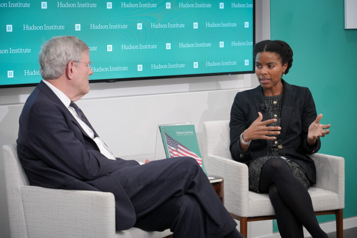 Olivia Trusty sits on a stage talking with Harold Furchtgott-Roth