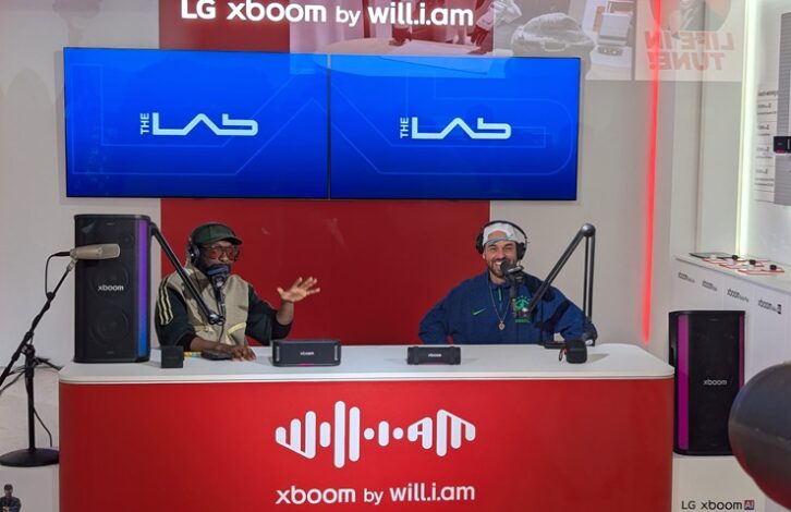Will.i.am and Bizarrap sit in an exhibit booth with microphones in front of them. 
