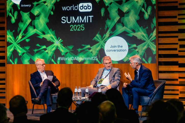 Three men sit on a stage at the WorldDAB Summit in 2025.