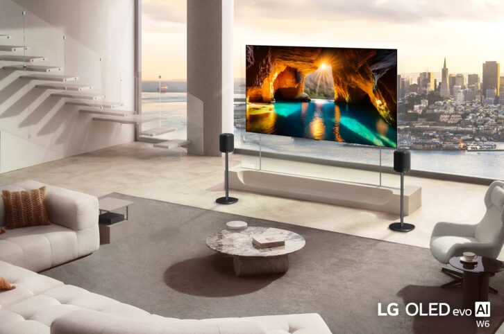 A large,, very thin TV screen is depicted in a bright airy room with a city skyline visible outside the windows