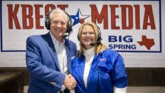 G. Brint Ryan and Malinda Flenniken shake hands in front of a KBest Media sign