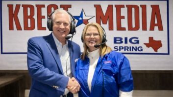 G. Brint Ryan and Malinda Flenniken shake hands in front of a KBest Media sign