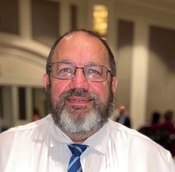 Steve Griesbach smiles at the camera. He wears a business shirt and tie, and has glasses and a beard.