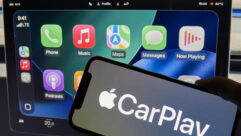 An iPhone showing Apple CarPlay is seen in front of a Tesla Model 3 screen
