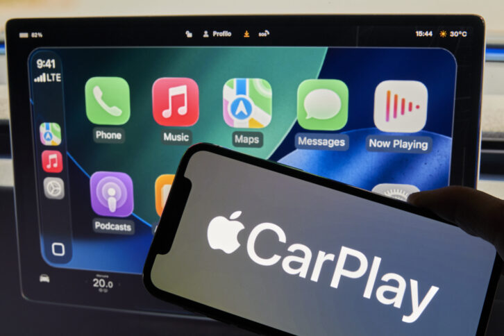 An iPhone showing Apple CarPlay is seen in front of a Tesla Model 3 screen