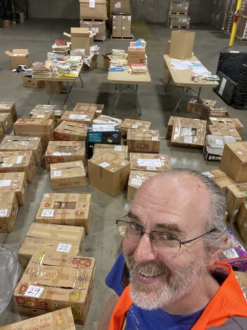 Kay poses with some of the 7 pallets of Bob Cooper material