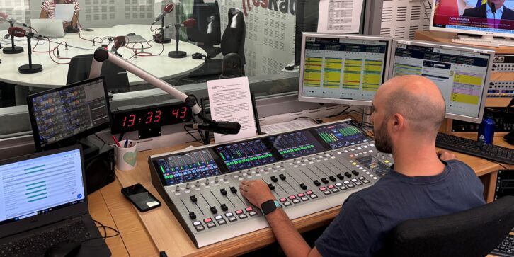 A view of a radio studio with a person sitting at a DHD audio console