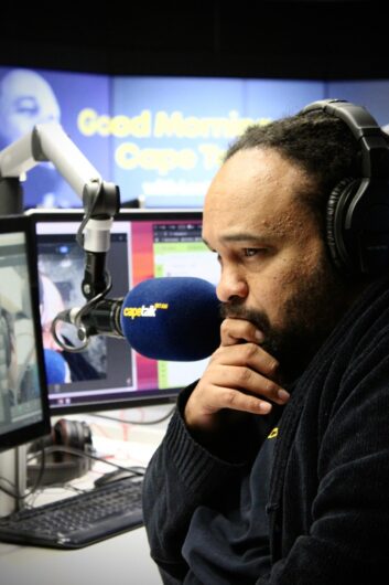 Lester Kiewit sits at a microphone listening on headsets to a caller