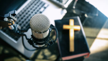 Closeup of a microphone in a studio, with a Bible and a cross visible under it on the tabletop