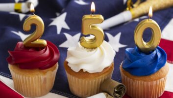Red, white and blue cupcakes with candles that spell out "250" sit against a backdrop of the American flag
