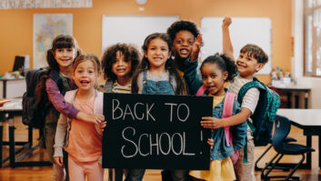 Back to school celebration. Excited elementary school class ready to learn on first day of class. Group of children smiling at the camera while holding a back to school sign in a classroom.