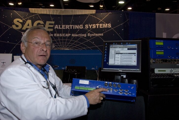 Jerry LeBow demonstrates equipment in the Sage booth while wearing a white lab coat