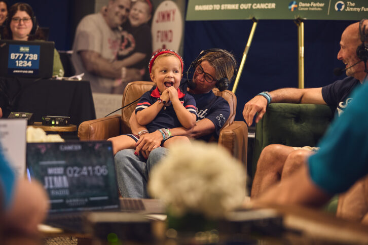 A Dana-Farber pediatric patient smiles on-air alongside loved ones during a live interview segment at Fenway Park.