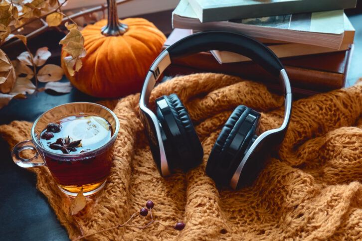 Audiobook or podcast in fall season. Wireless headphones with books and autumn leaves on knitted plaid as concept of learning and education, online courses or music app in cozy fall mood.