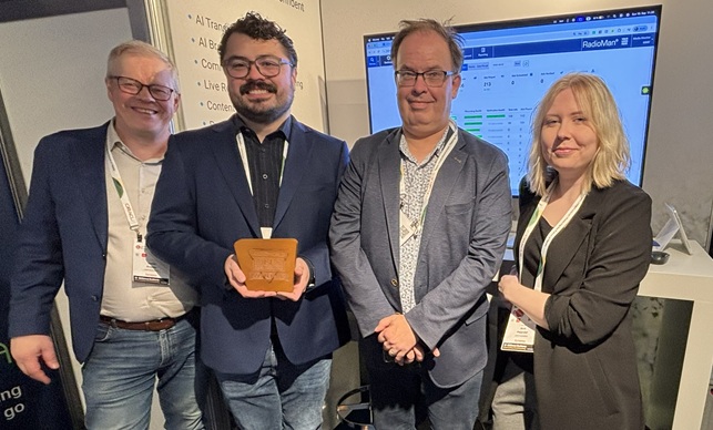 Four people stand in the Jutel booth at the IBC Show with an award