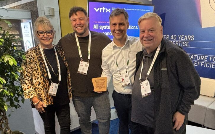 Four people in the On Air Solutions booth at IBC with an award