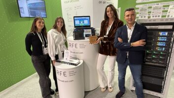 Four people stand in the RFE booth at IBC, one holds an award