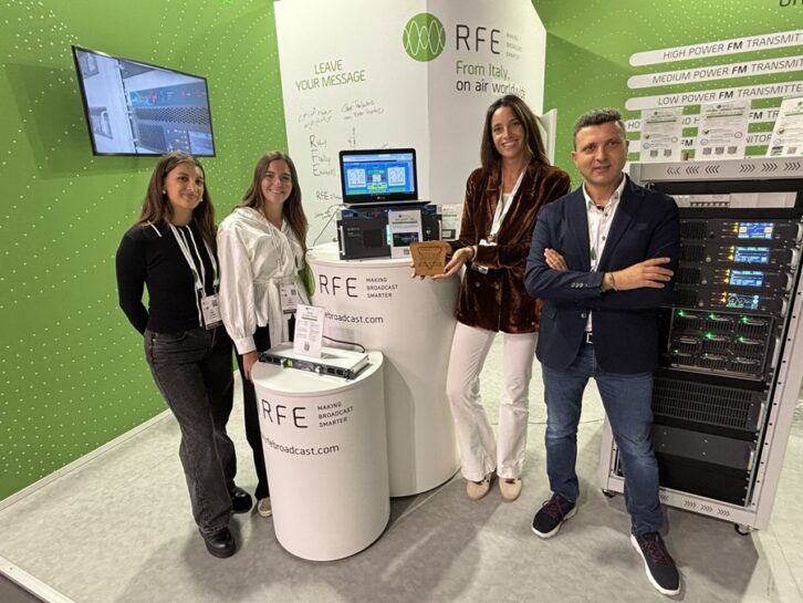 Four people stand in the RFE booth at IBC, one holds an award